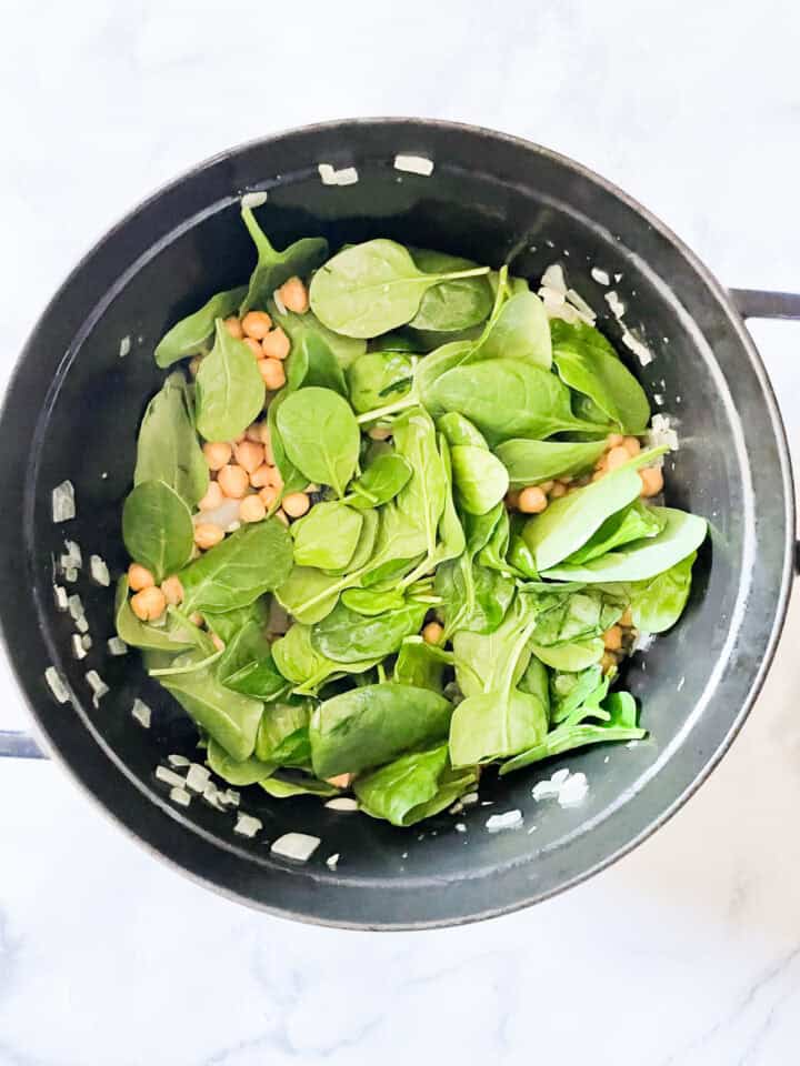 Spinach leaves are added to a pot of chickpeas.