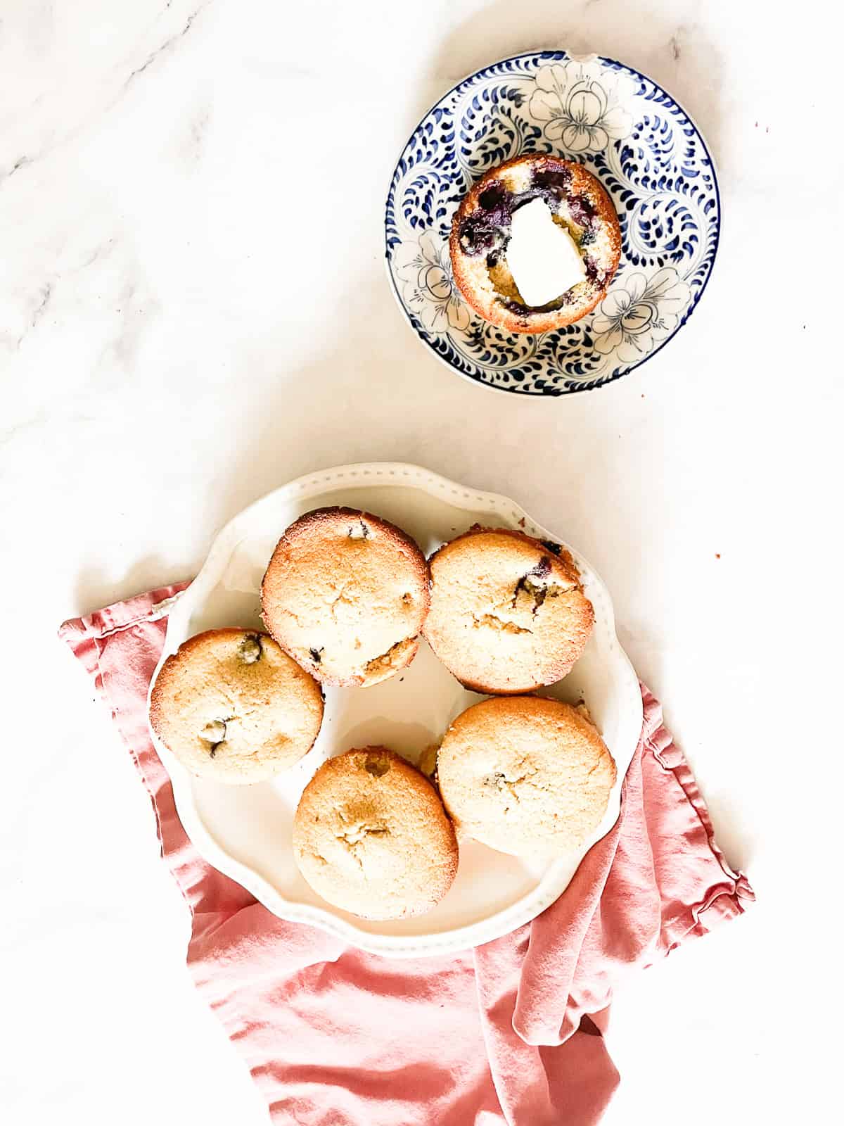 A gf blueberry muffin on a plate next to a plate of muffins.