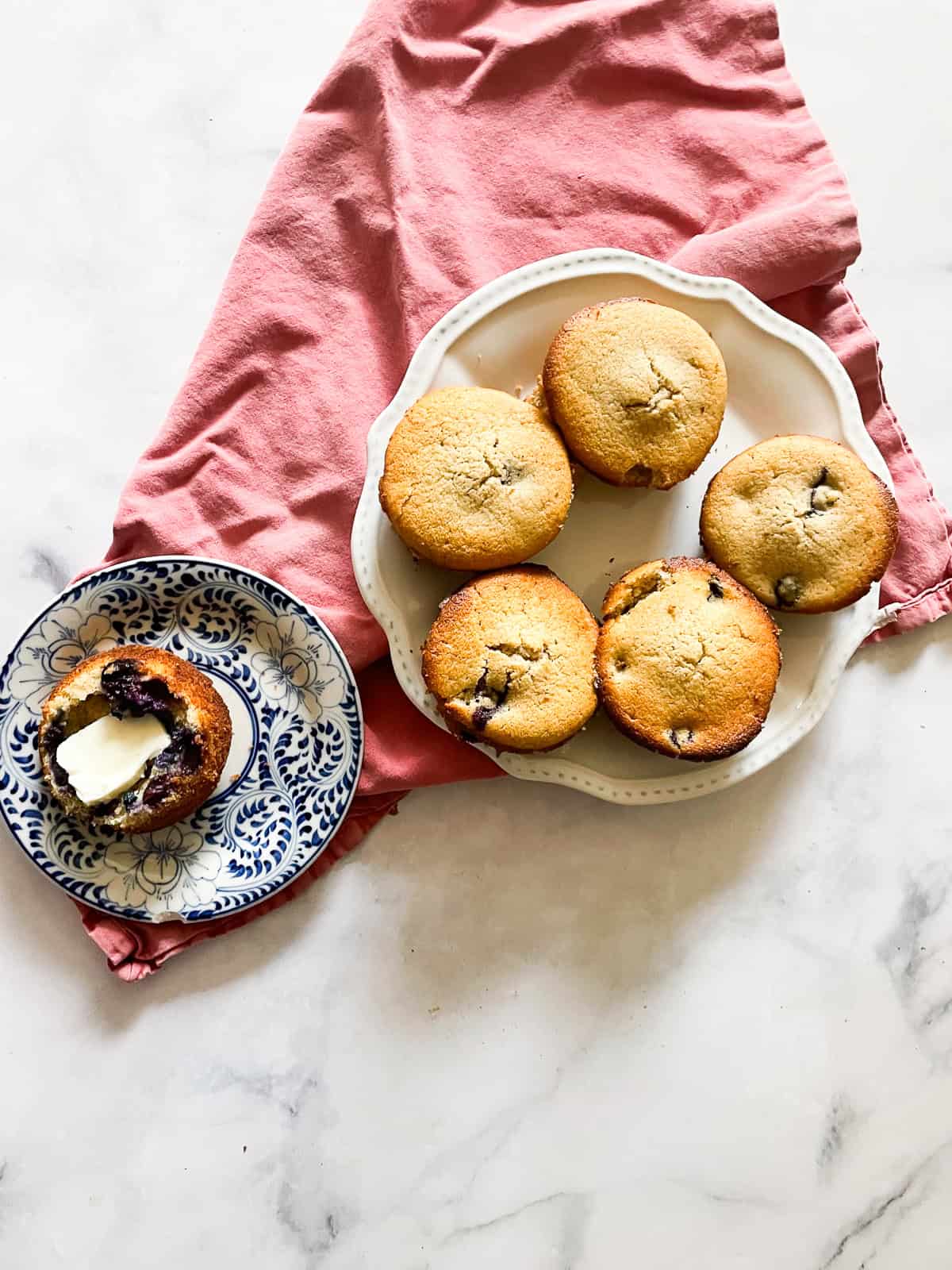 A plate of gf blueberry muffins with a muffin on a plate on a red napkin.