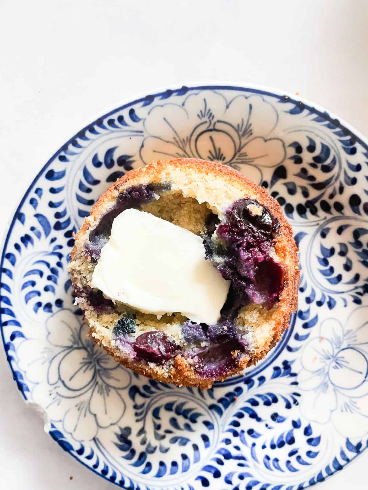 Half of a gf blueberry muffins with butter on a plate.