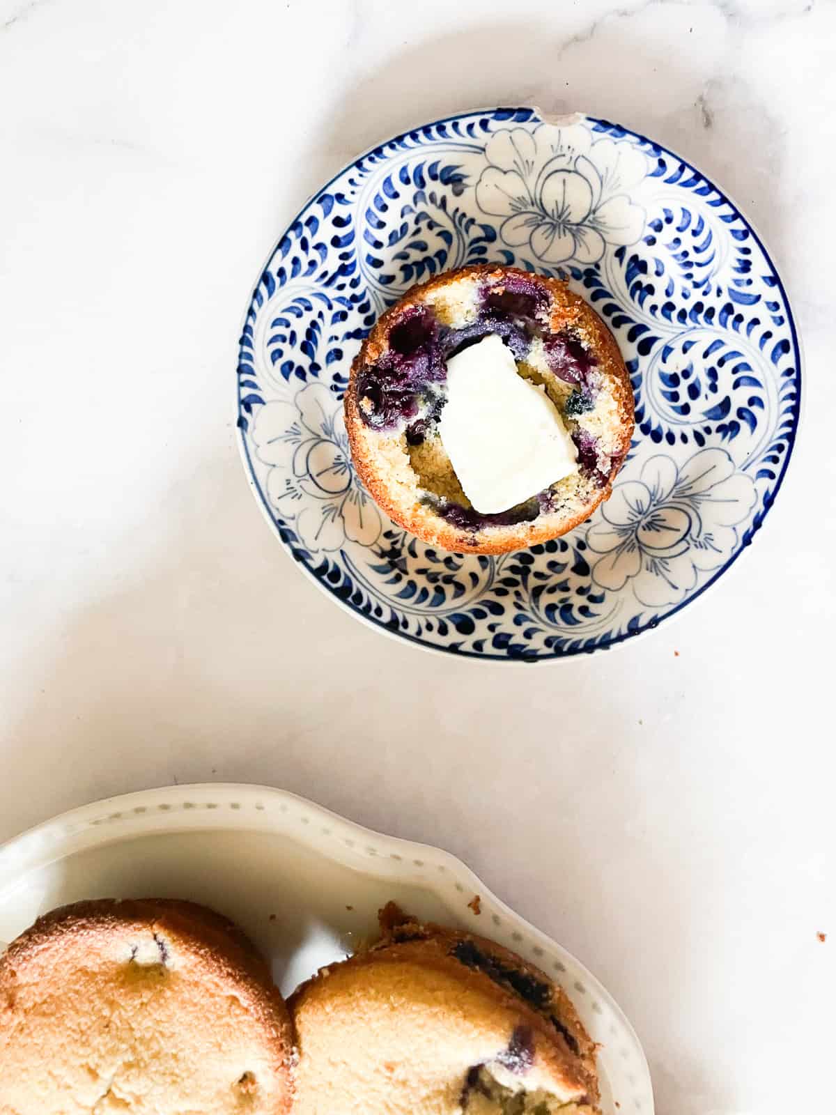 A pat of butter on a gf blueberry muffin on a plate.