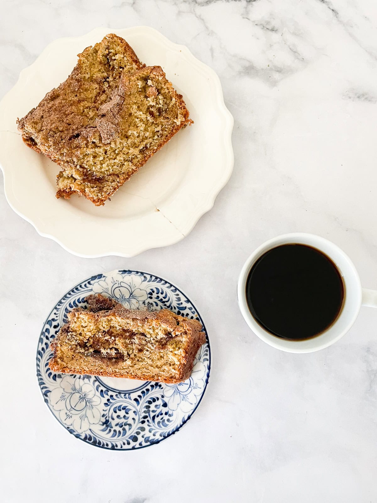 A slice of cinnamon swirl bread on a blue and white plate with a plate with more slices near it and a cup of coffee.