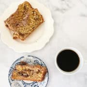 A slice of cinnamon swirl bread on a blue and white plate with a plate with more slices near it and a cup of coffee.