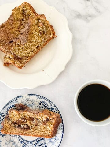 A slice of cinnamon swirl bread on a blue and white plate with a plate with more slices near it and a cup of coffee.