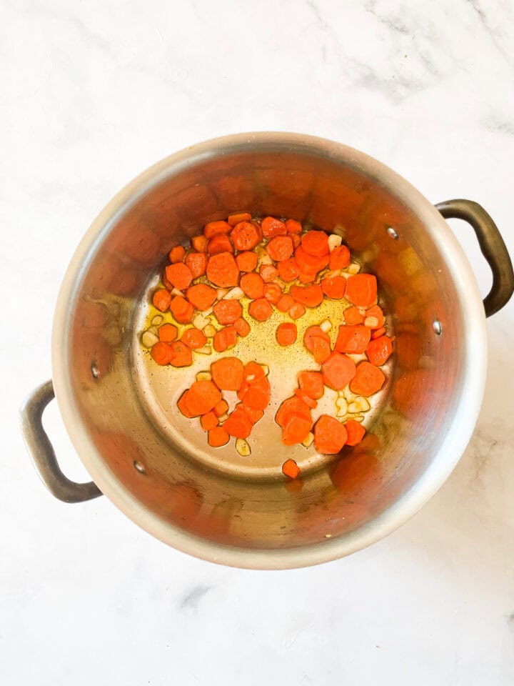 Carrots and garlic cook in olive oil in a pot.