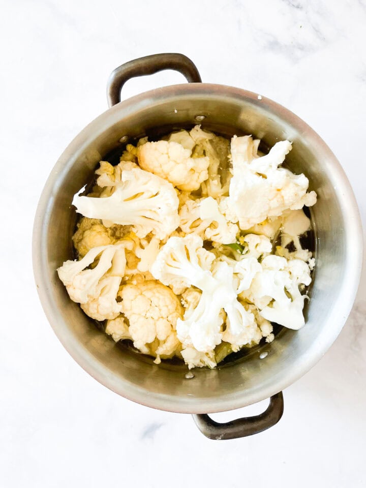 Cauliflower is added to a soup pot.