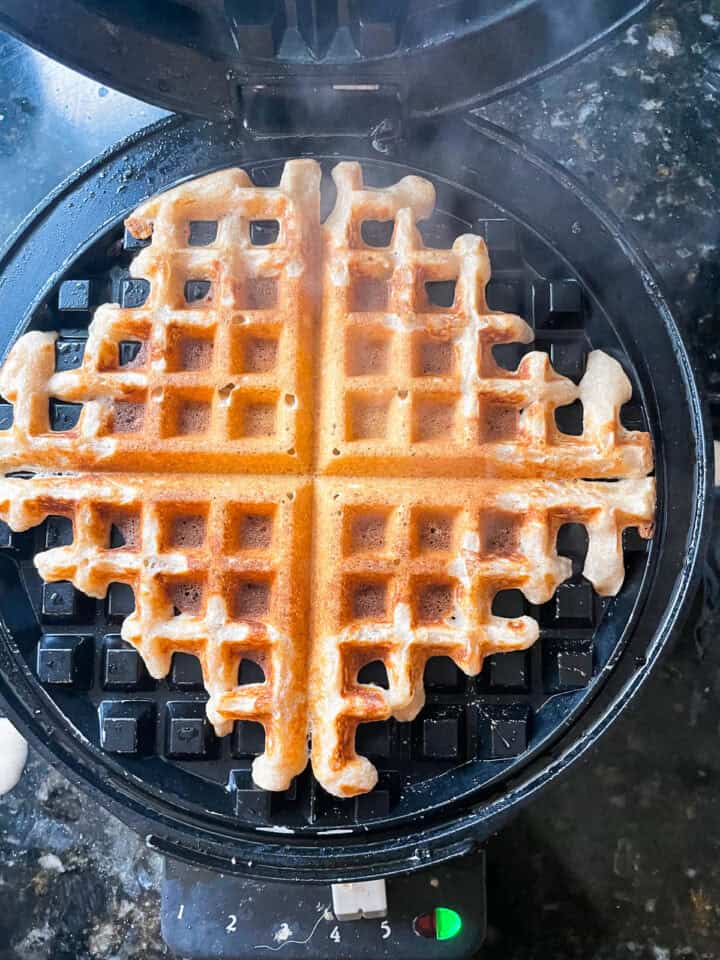 A waffle cooks on a waffle iron.