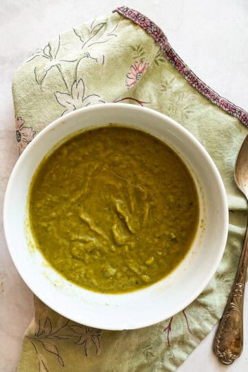 A bowl of asparagus potato soup with a spoon on a green napkin.