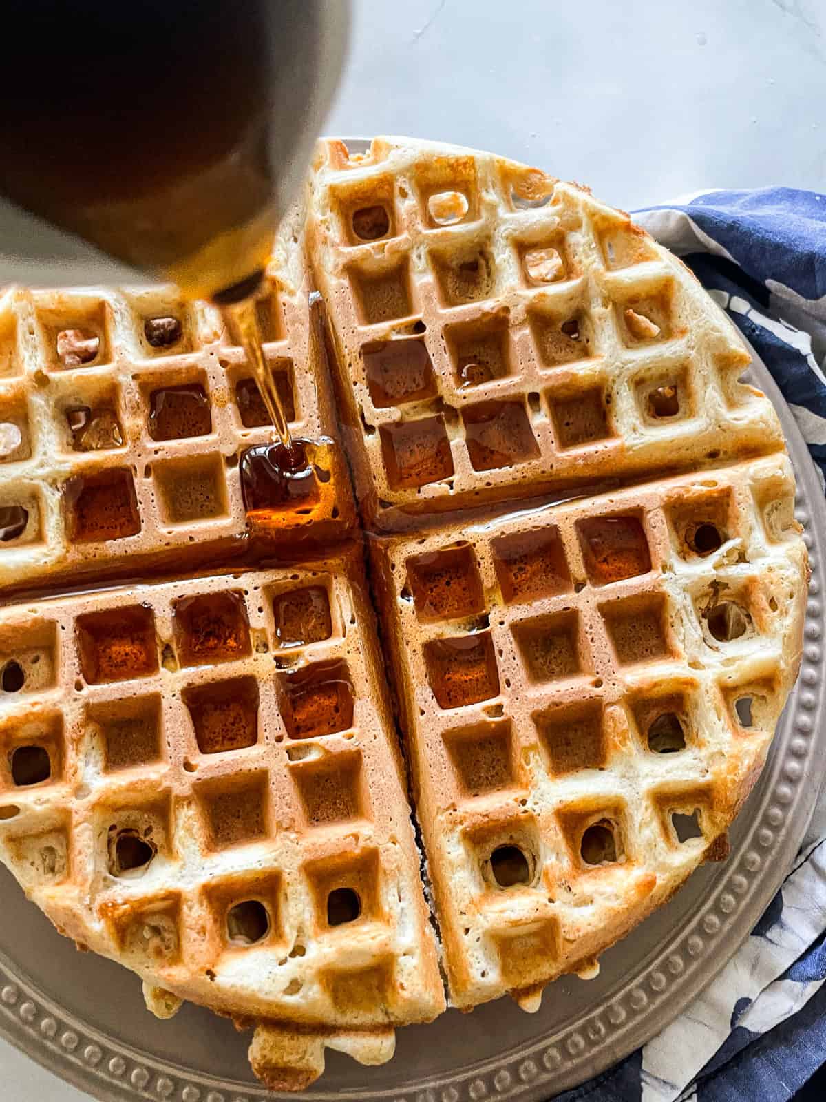 Maple syrup is poured onto waffles from a pitcher.