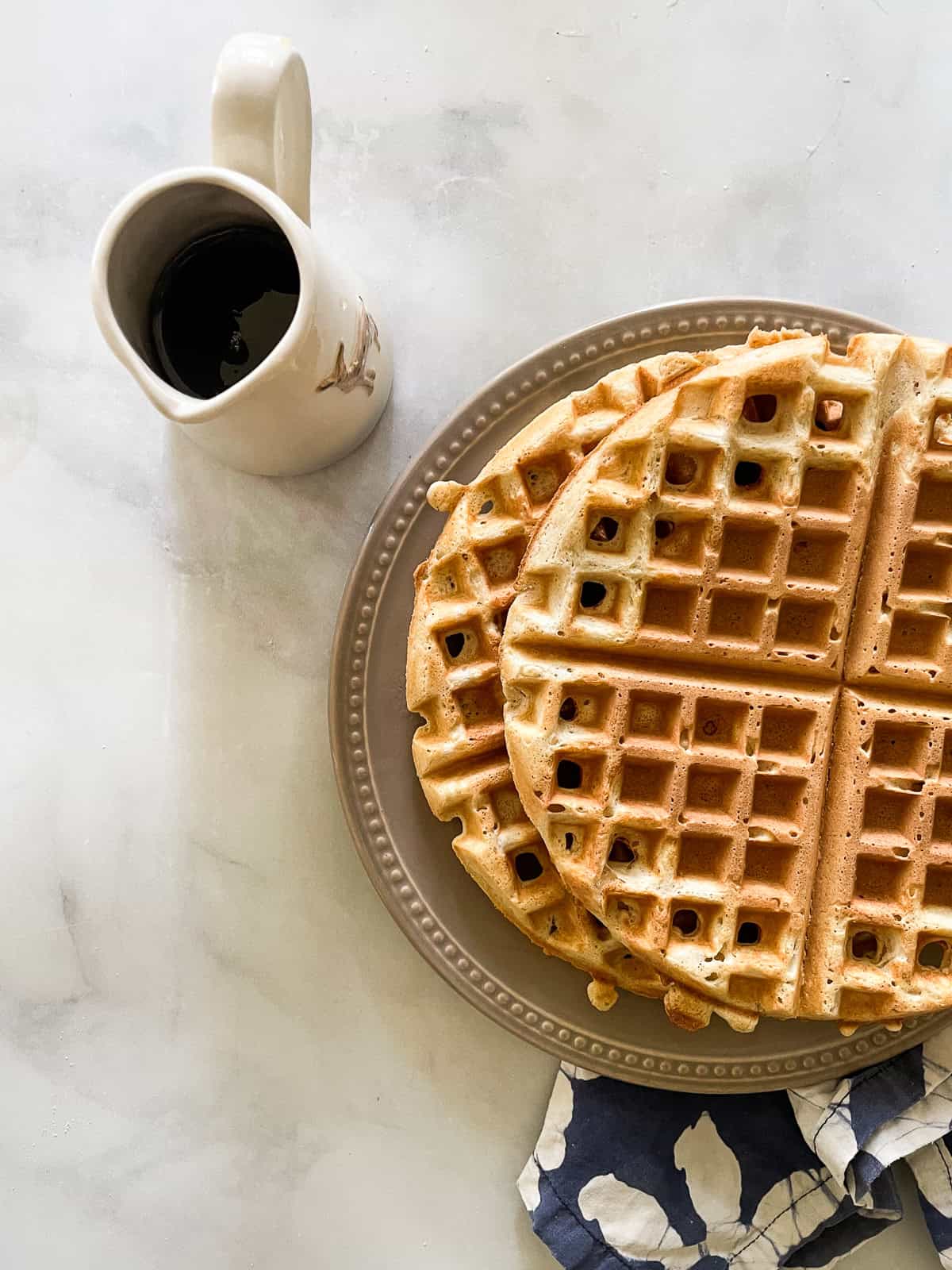 Waffles on a plate with a pitcher of syrup.