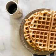 Waffles on a plate with a pitcher of syrup.