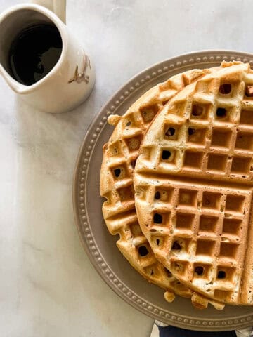 Waffles on a plate with a pitcher of syrup.