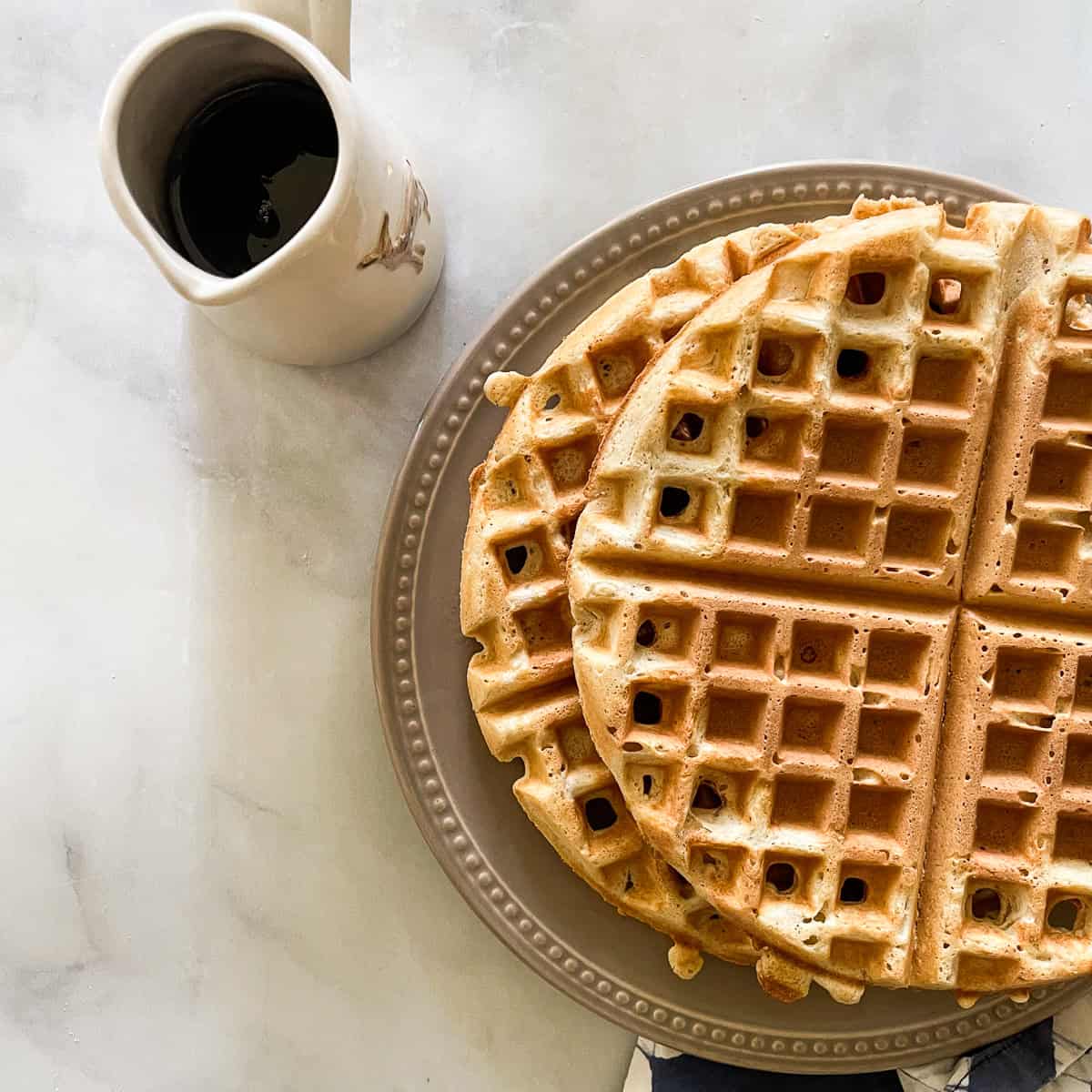 Waffles on a plate with a pitcher of syrup.