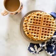Waffles on a plate with a cup of coffee.
