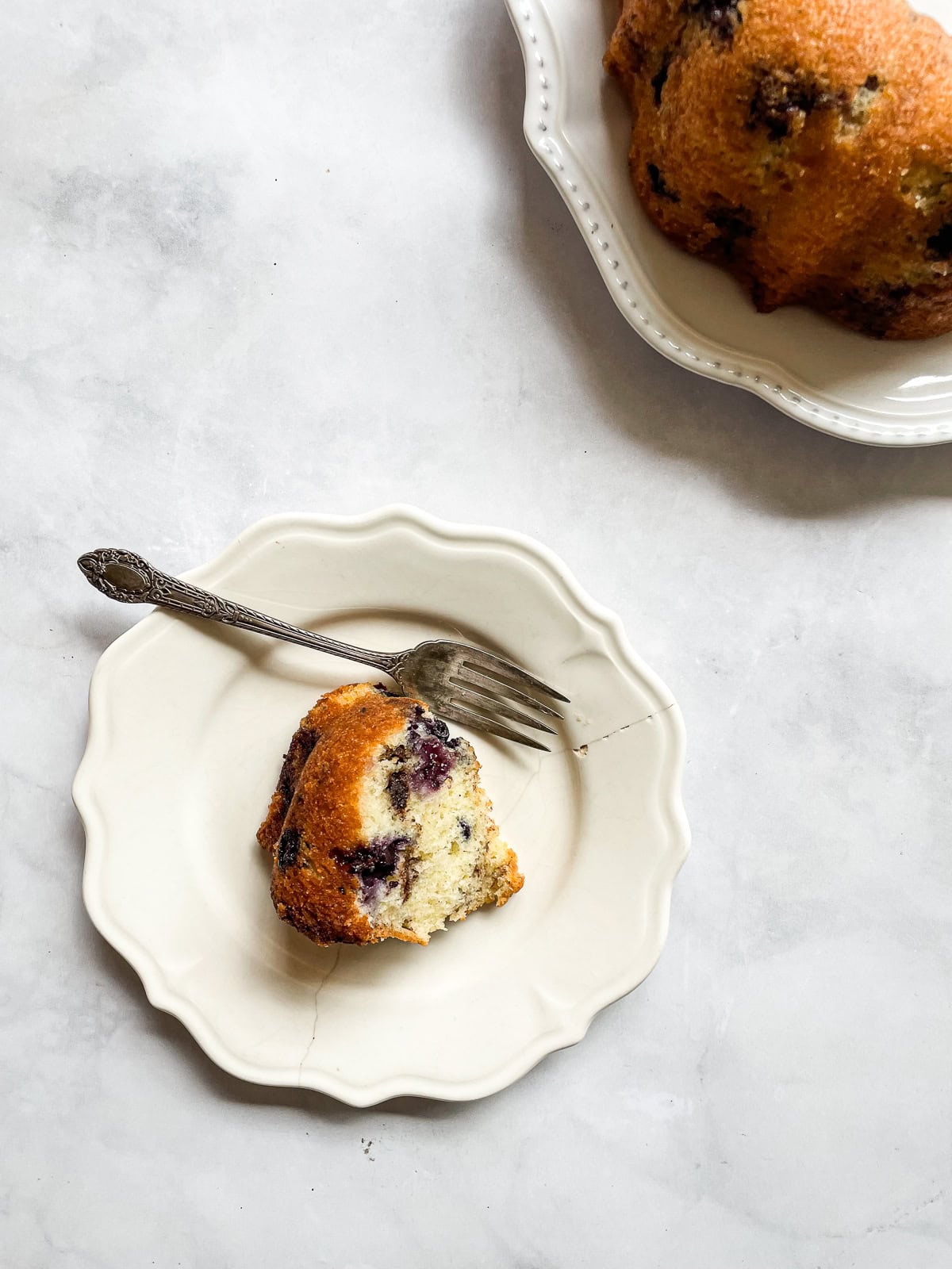 A slice of blueberry yogurt cake on a plate with a fork and the cake next to it.