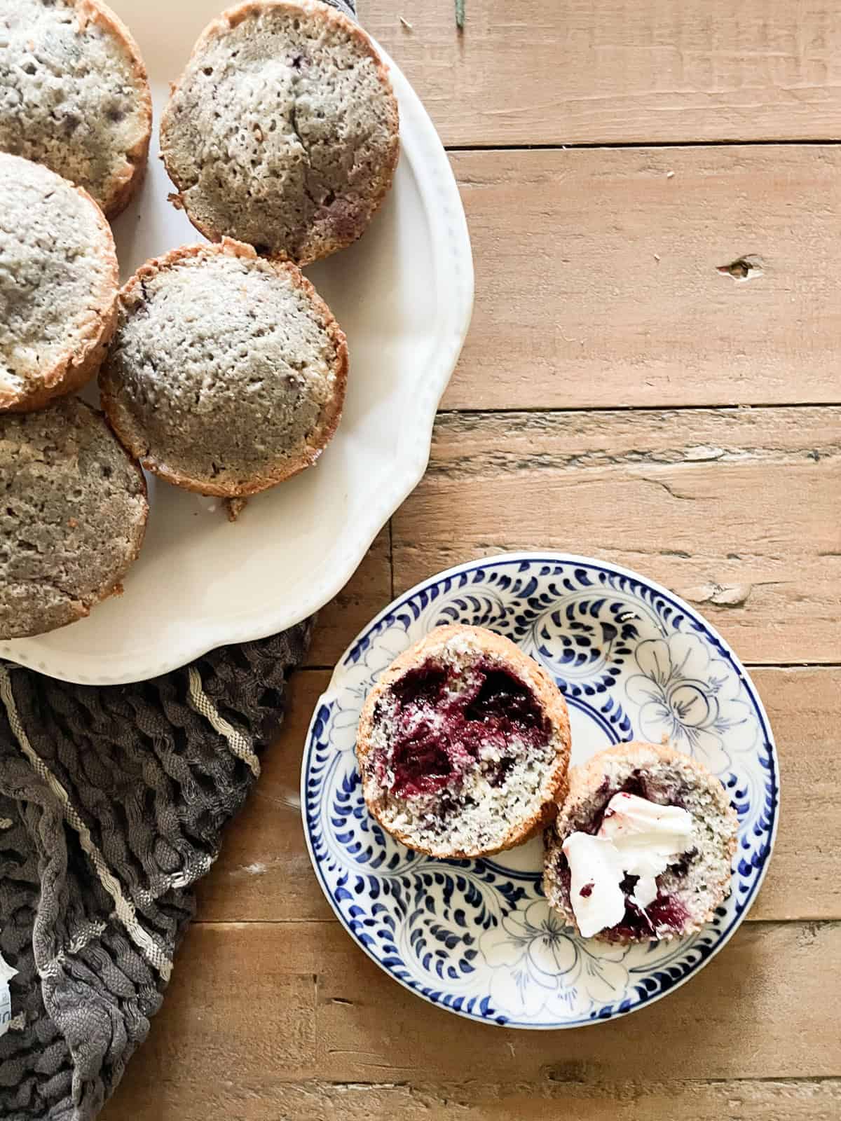 A gluten-free blackberry muffin with butter next to a plate of muffins.