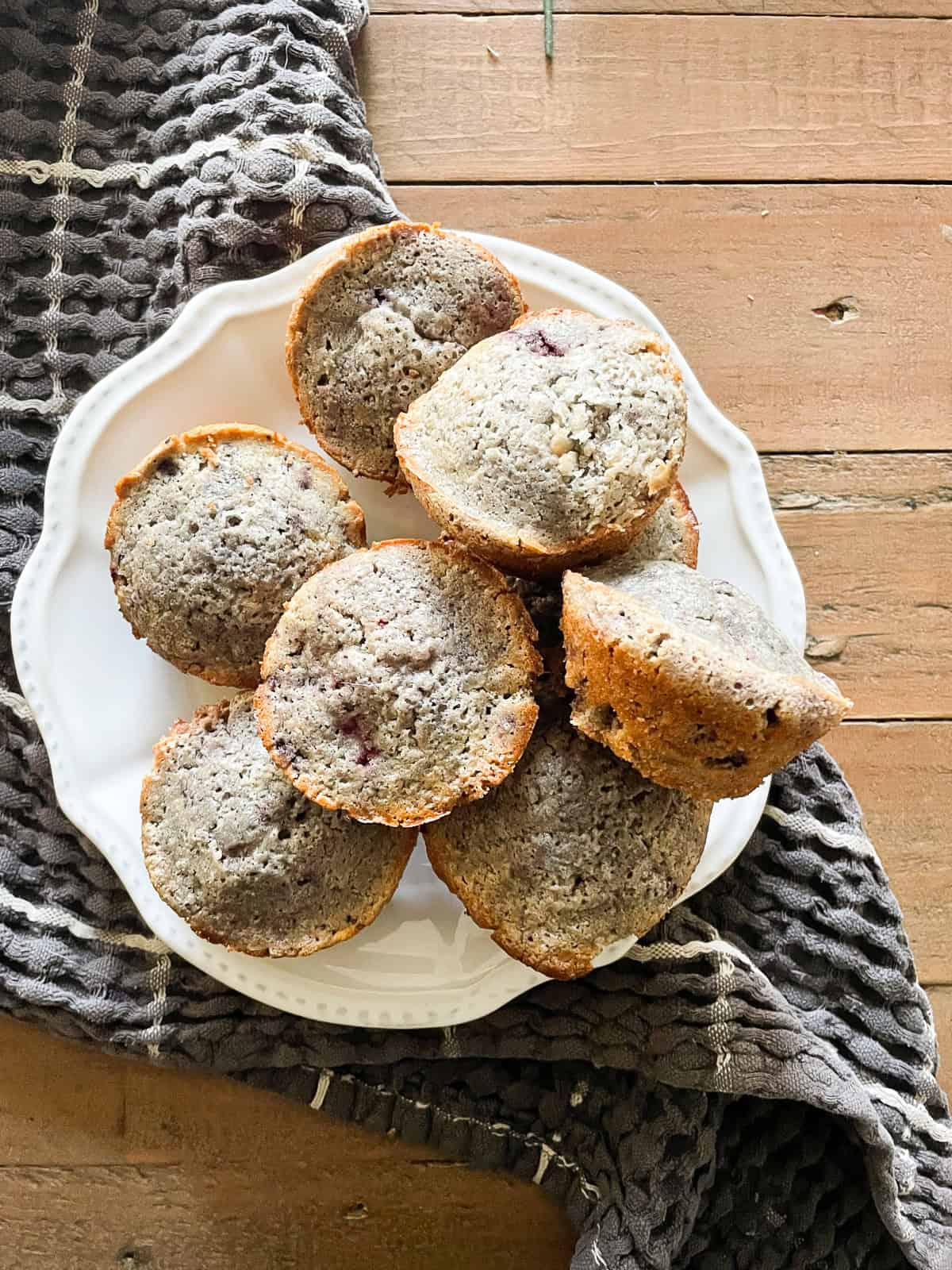 A blue towel underneath a plate of gluten-free blackberry muffins.