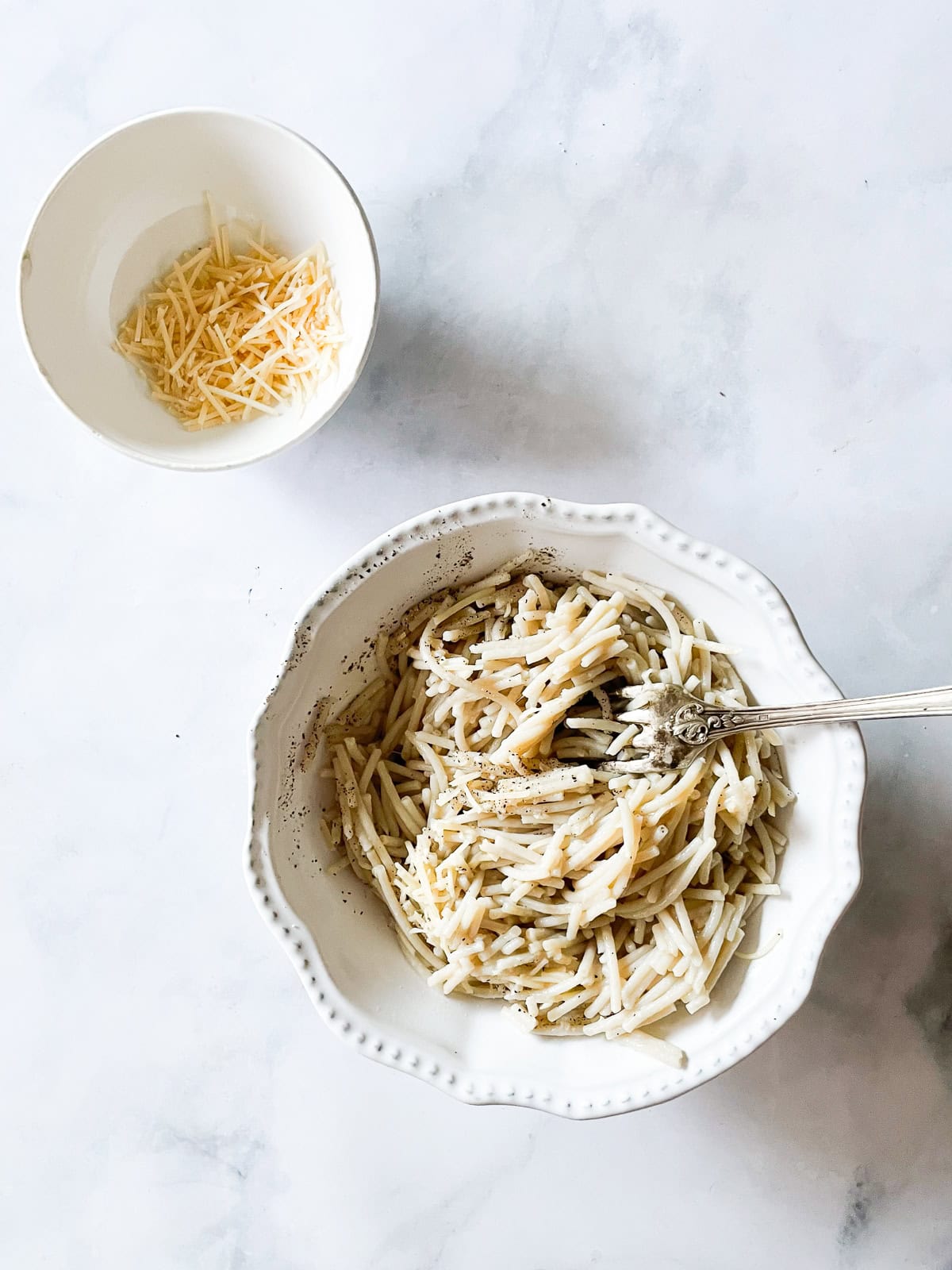 A bowl of cheesy pasta with a bowl of cheese next to it.