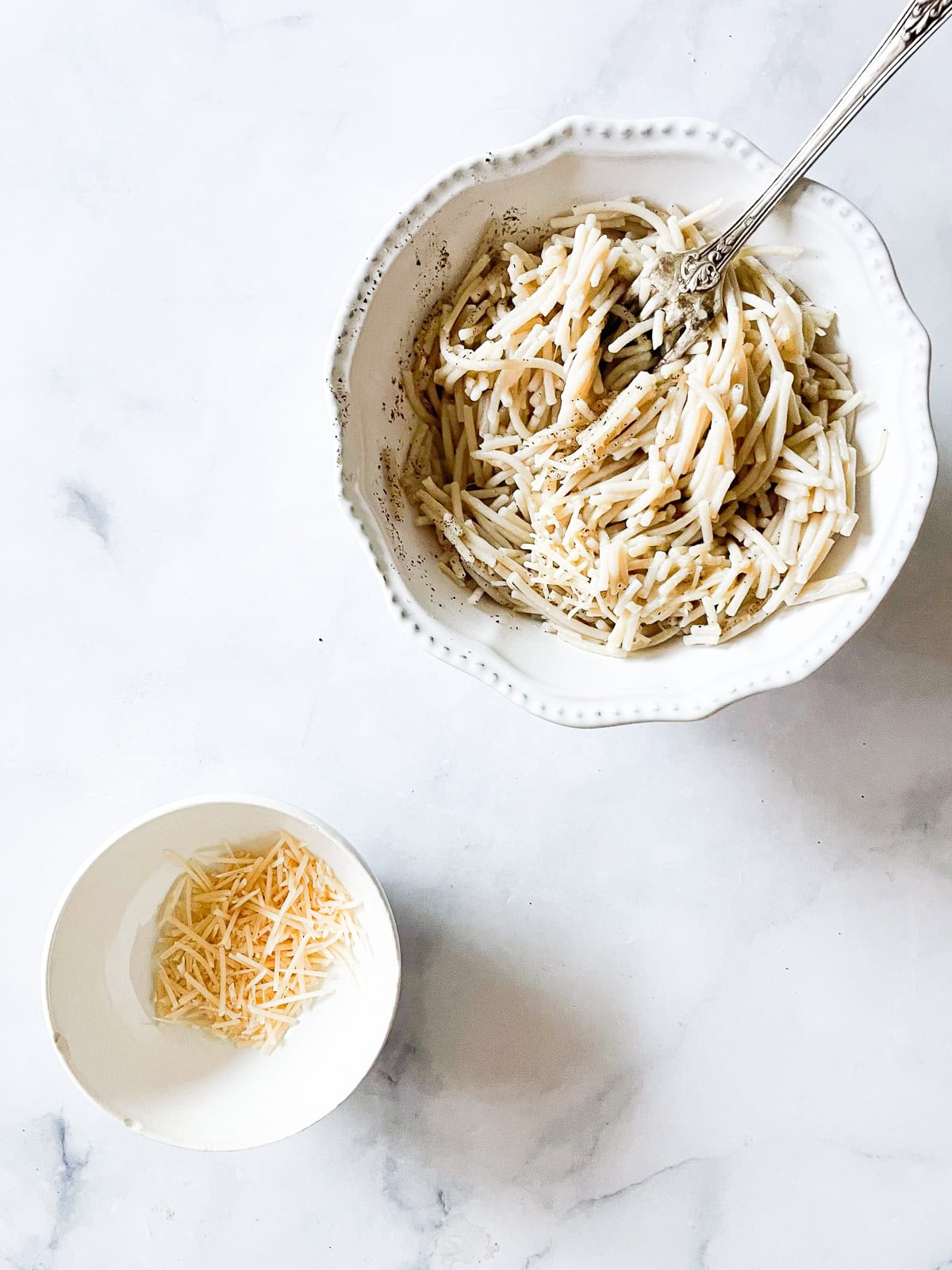 A bowl of cheesy pasta with a bowl of cheese next to it.