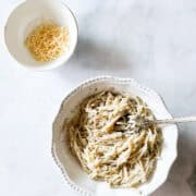 A bowl of cheesy pasta with a bowl of cheese next to it.