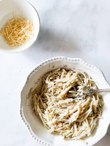 A bowl of cheesy pasta with a bowl of cheese next to it.