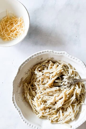 A bowl of cheesy pasta with a bowl of cheese next to it.