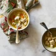 Two bowls of gluten free chicken soup with spoons near a napkin.