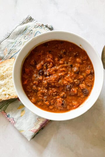 A bowl of gluten free chili with a slice of bread and a spoon.