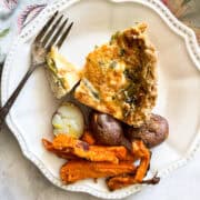 A plate with a slice of gluten free quiche, a fork, and vegetables.