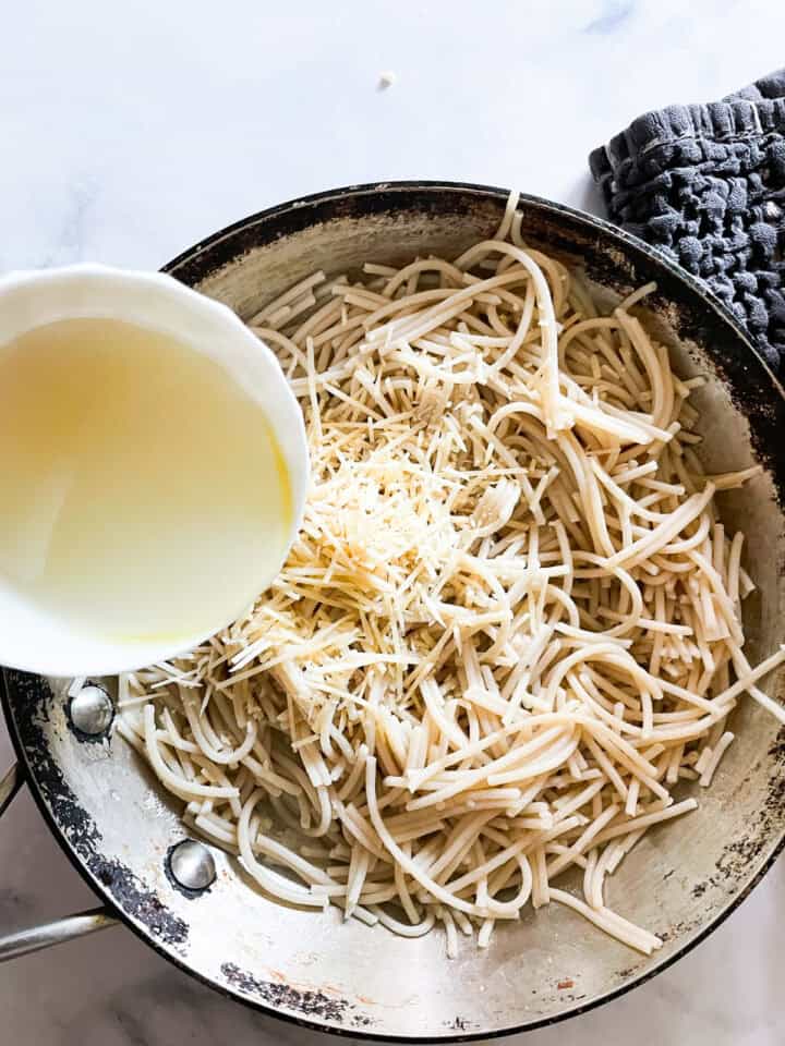 A little pasta water is added to a skillet of cheesy pasta.