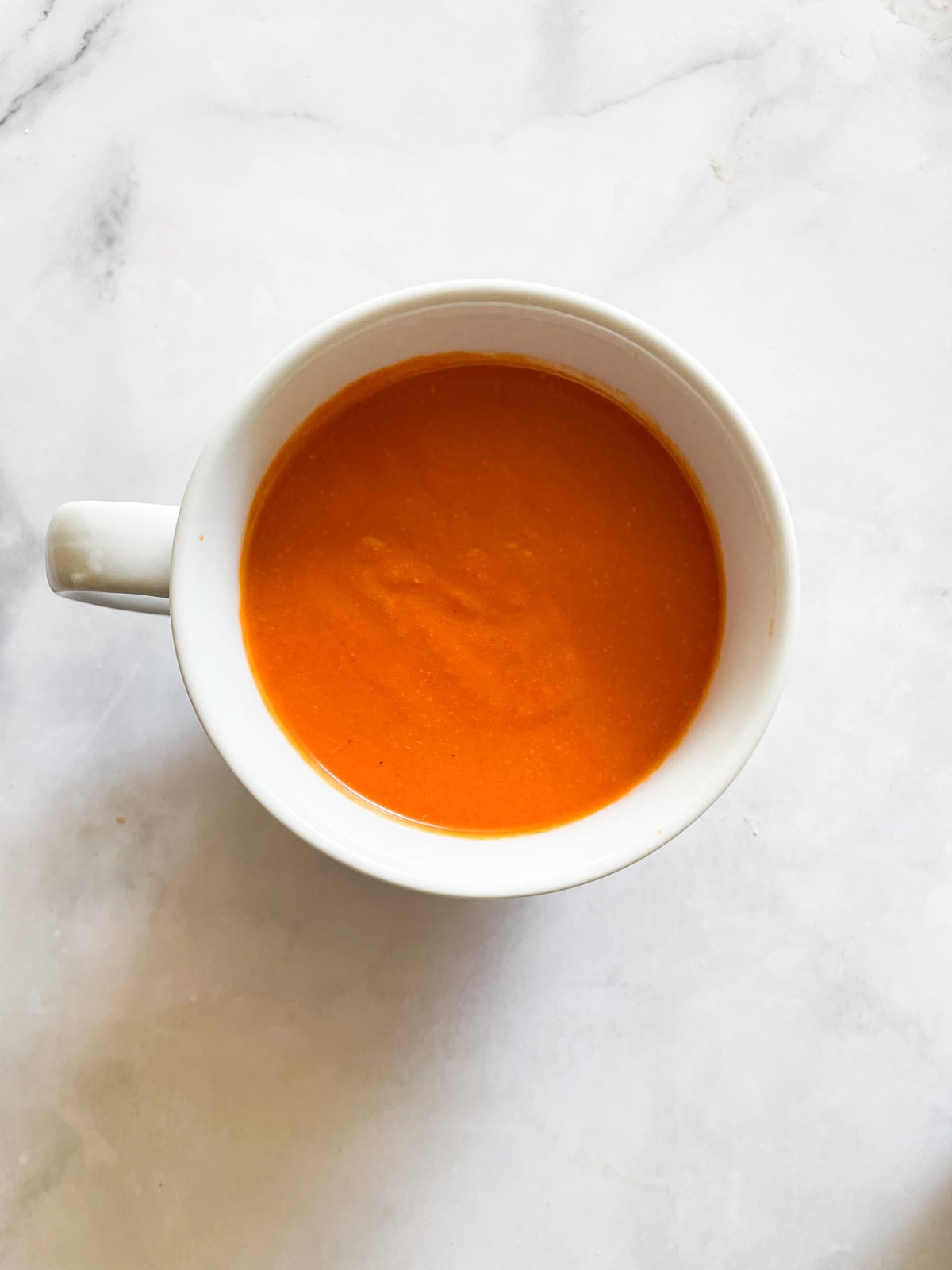 A white cup of cream of tomato soup.