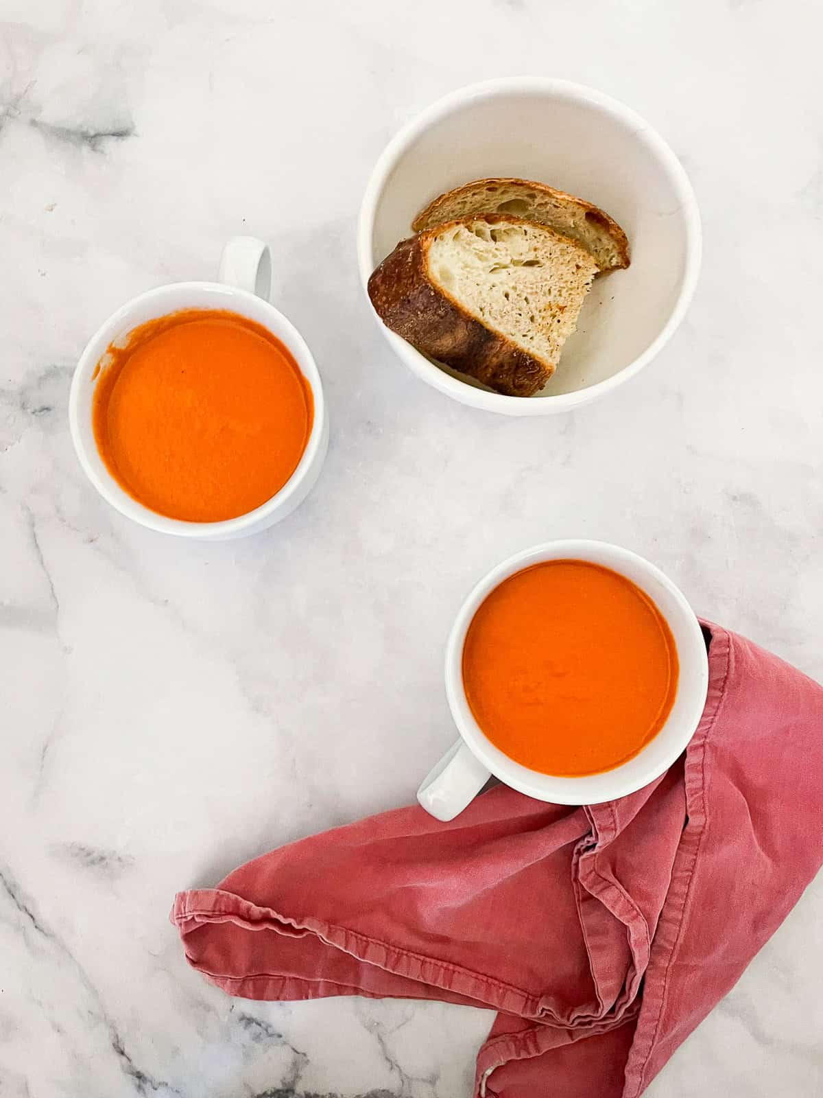 Cups of vegetarian cream of tomato soup with a bowl of bread.