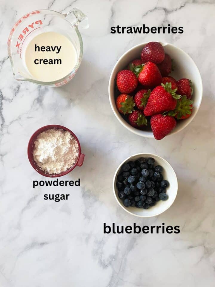 A gluten free berries and cream cake is layered with sweet whipped cream, sliced strawberries, and juicy blueberries. Ingredients for berries and cream cake topping are text-labeled.