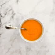 A small bowl of carrot & coconut soup with a spoon.