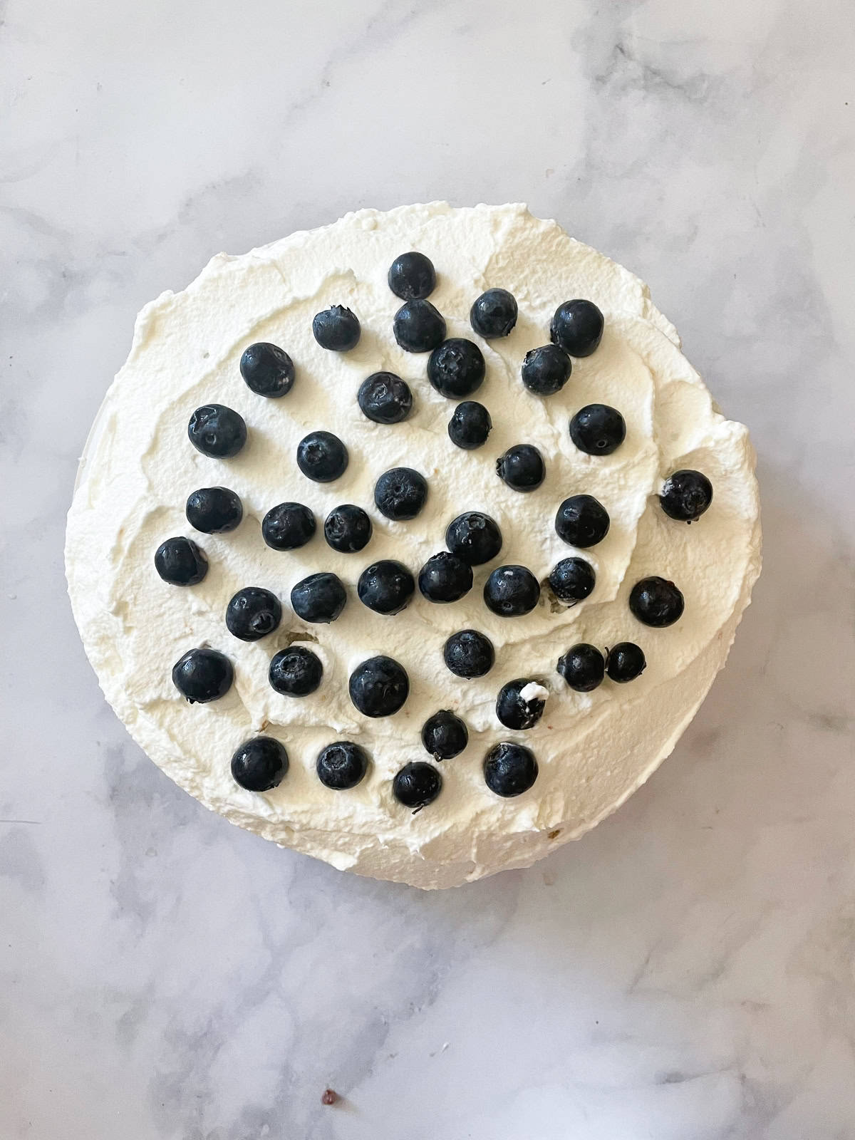 A gluten free berries and cream cake is layered with sweet whipped cream, sliced strawberries, and juicy blueberries. Blueberries decorate the top of a berries and ream cake.