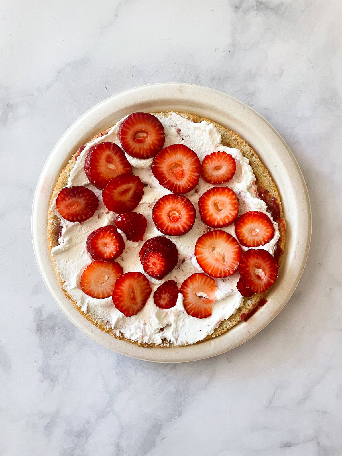 A gluten free berries and cream cake is layered with sweet whipped cream, sliced strawberries, and juicy blueberries. Strawberrues are added to whipped cream.