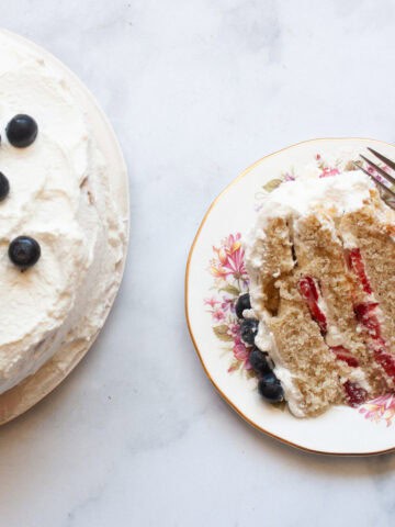 A slice of berries and cream cake on a plate with a fork next to the cake.