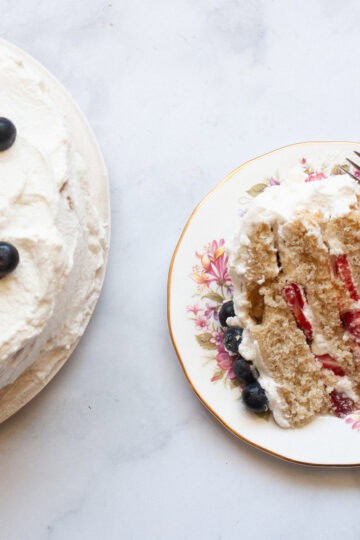 A slice of berries and cream cake on a plate with a fork next to the cake.