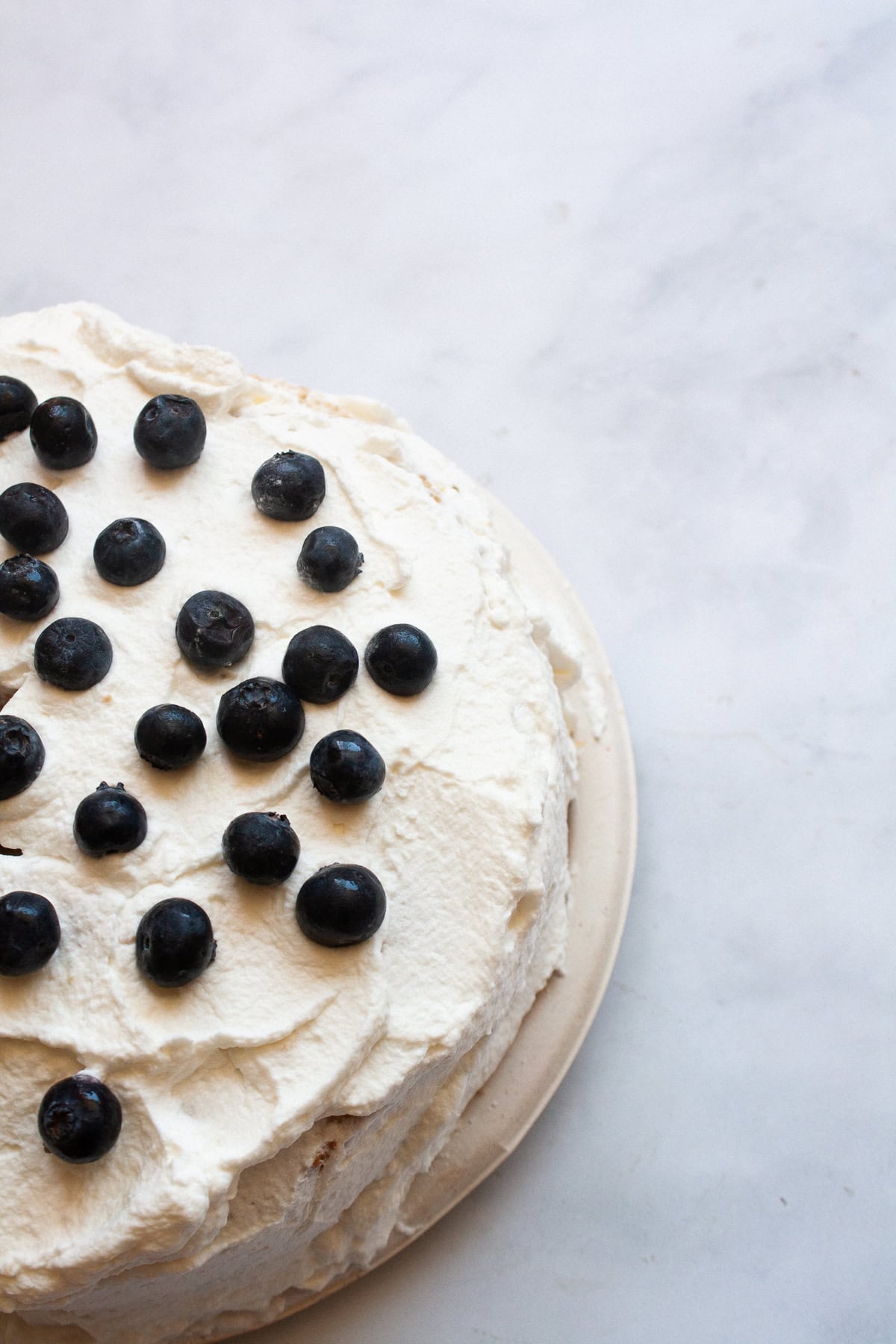 A gluten free berries and cream cake is layered with sweet whipped cream, sliced strawberries, and juicy blueberries. Blueberries top a cream cake.