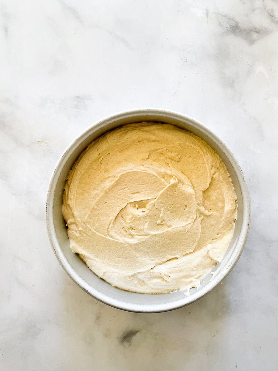 A gluten free berries and cream cake is layered with sweet whipped cream, sliced strawberries, and juicy blueberries. Butter cake batter in a baking round.