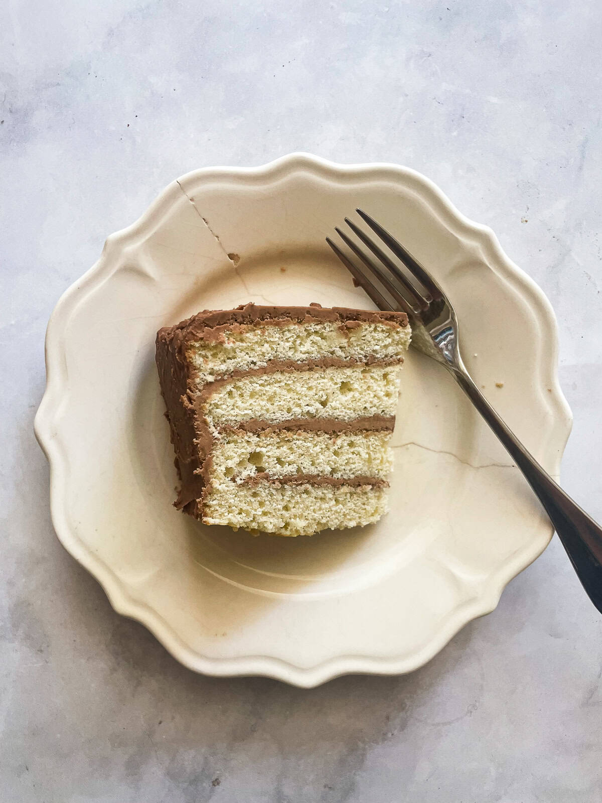 This beautiful gluten-free birthday cake recipe features velvety vanilla cake layers filled and frosted with chocolate buttercream frosting A slice of cake on a plate with a fork.
