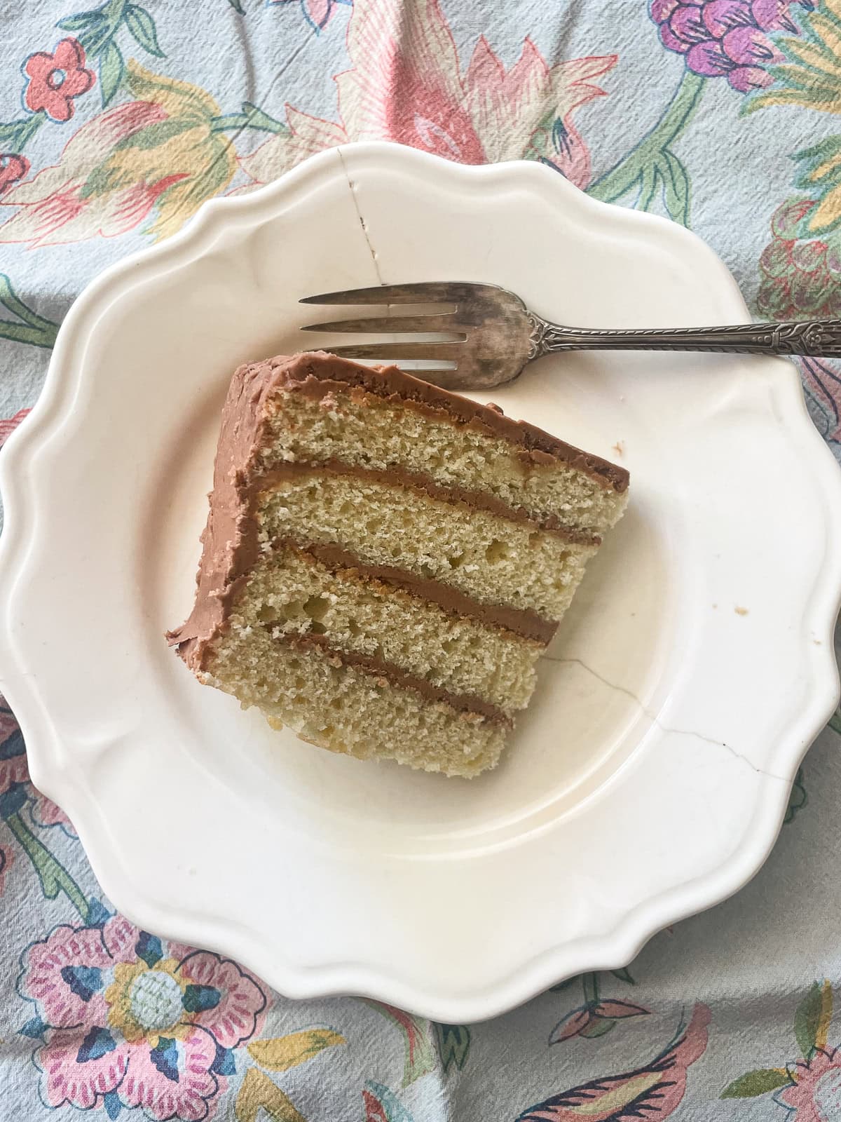 This beautiful gluten-free birthday cake recipe features velvety vanilla cake layers filled and frosted with chocolate buttercream frosting A plate with a slice of gluten-free birthday cake on a napkin.