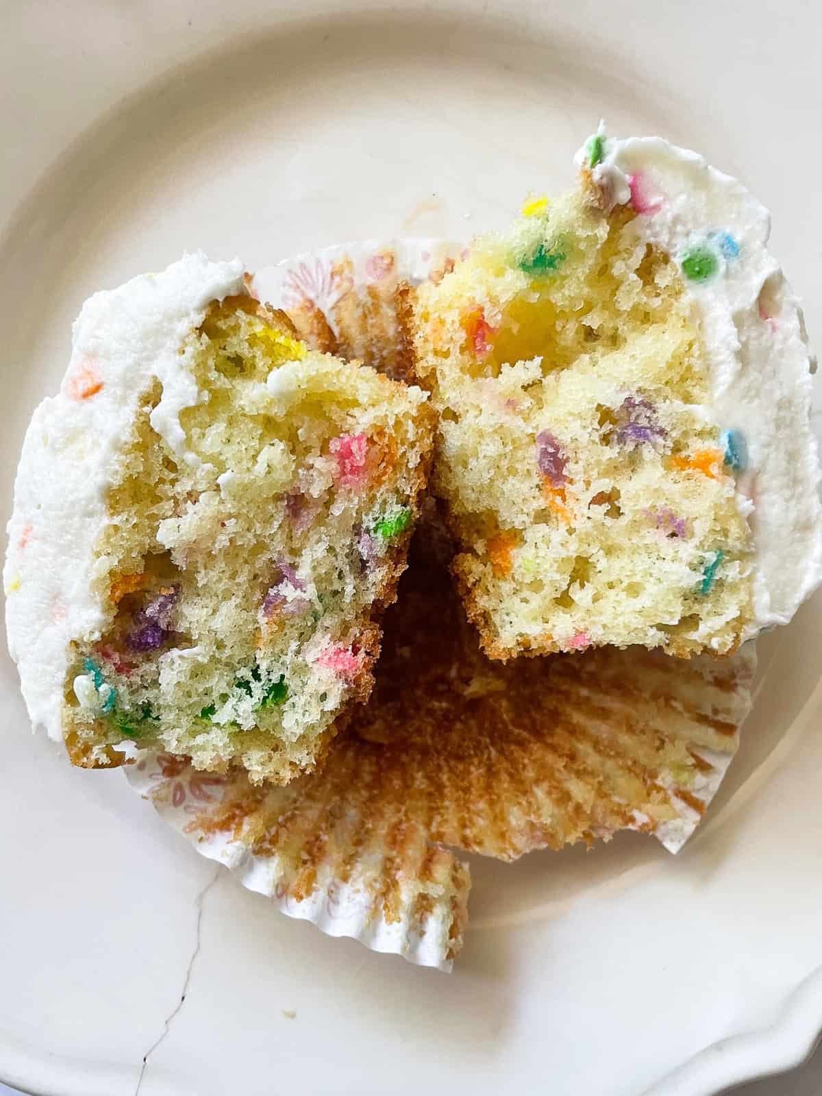 A gluten free funfetti cupcake cut in half on a plate.