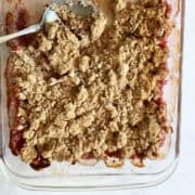 A spoon in a pan of gluten free rhubarb crumble.