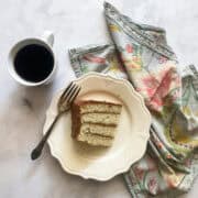 A slice of vanilla buttermilk cake on a plate with a cup of coffee.