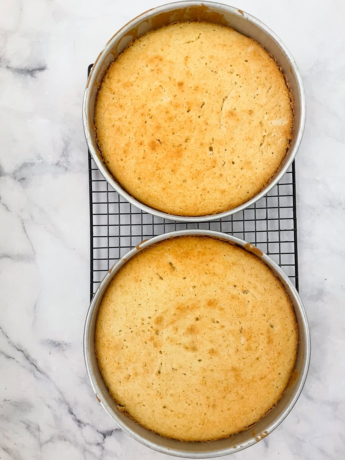 This beautiful gluten-free birthday cake recipe features velvety vanilla cake layers filled and frosted with chocolate buttercream frosting Two cake tins of gluten-free birthday cake cool on a rack.