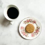 An oat flour peanut butter cookie on a plate next to a cup of coffee.