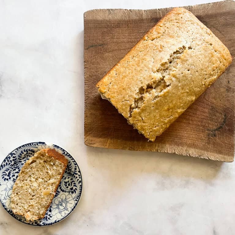 A slice of coconut loaf cake on a plate with the loaf next to it.
