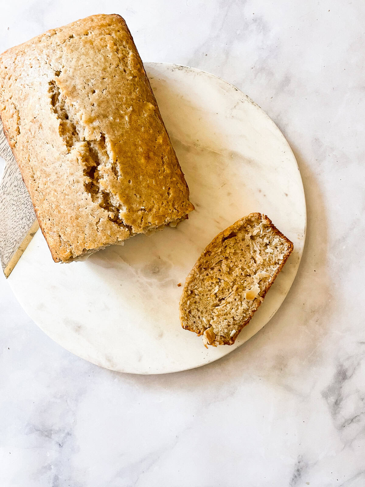 This lovely gluten free coconut loaf cake is jam-packed with chewy flaked coconut for a tropical touch. Inspired by our years in Australia. A loaf of gluten free coconut loaf cake with a slice cut from it.