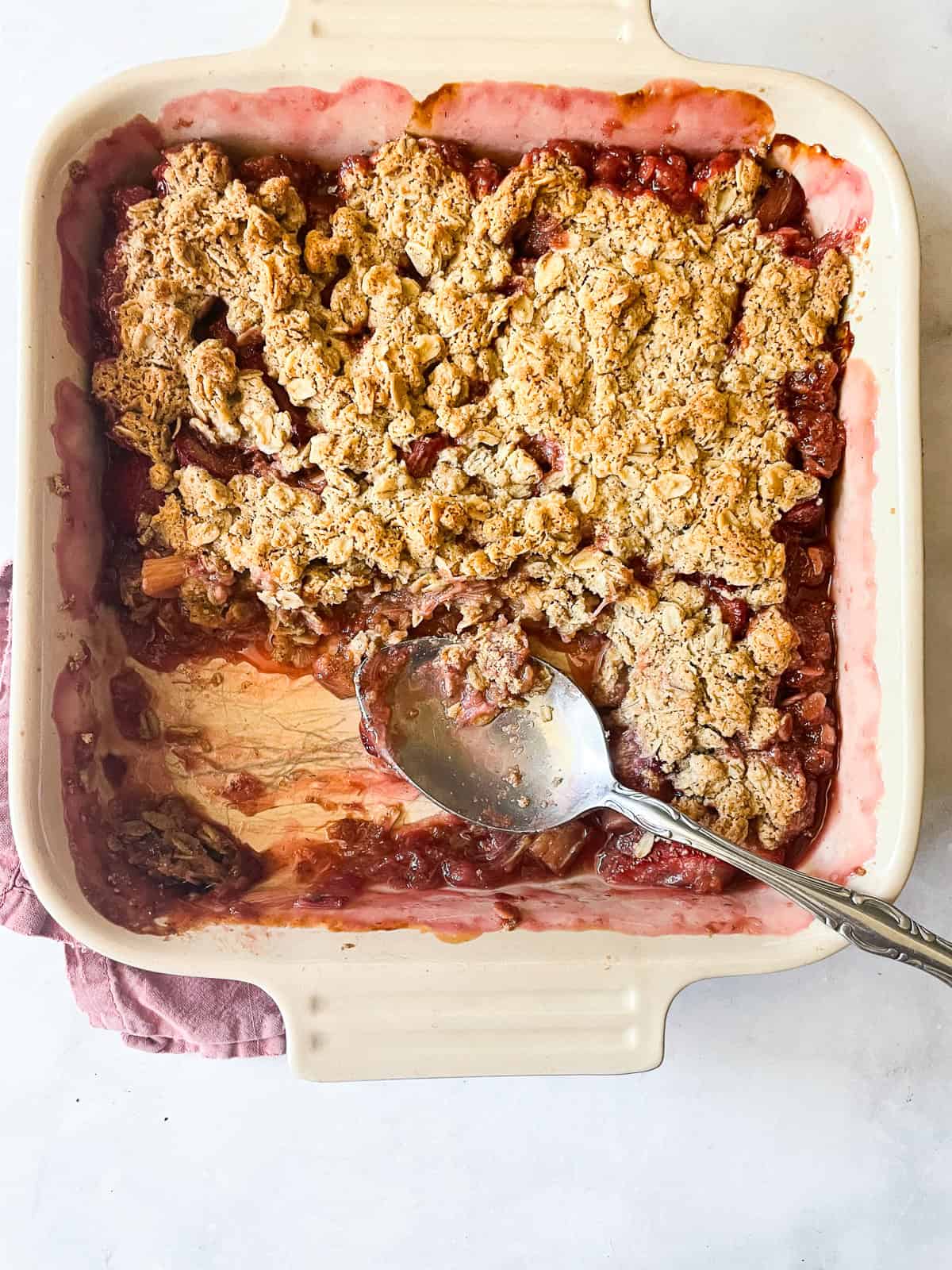 Sweet-tart rhubab is tucked under a buttery oat blanket in this classic gluten-free rhubarb crisp. Easily made dairy-free if needed. A pan of gluten-free rhubarb crisp with a spoon.